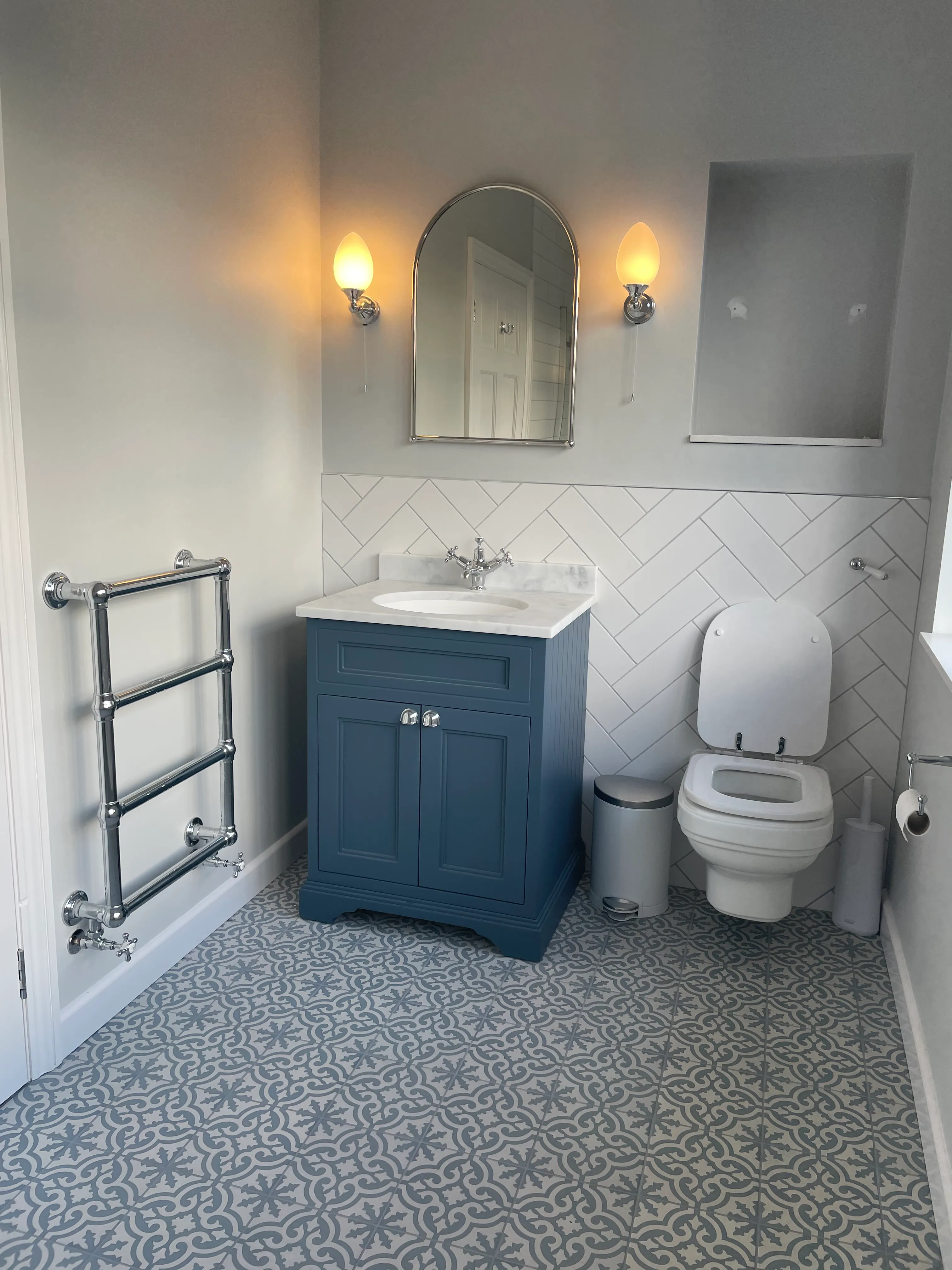 Traditional bathroom with patterned tile flooring, blue vanity unit, and chrome towel rail.