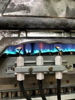 Gas boiler burner with blue flame and ignition electrodes during operation.