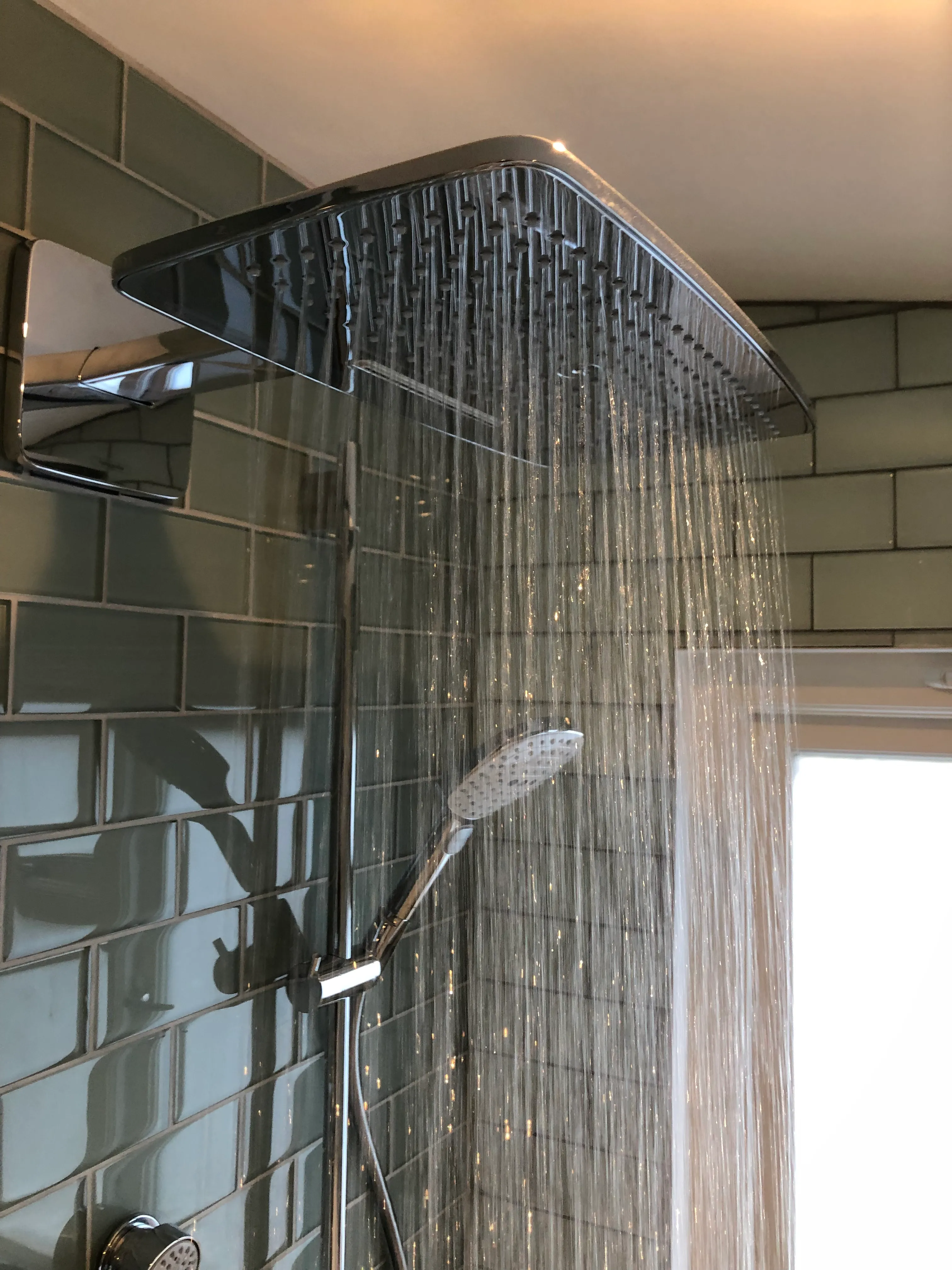 Modern rainfall shower head with running water in a tiled bathroom installation.